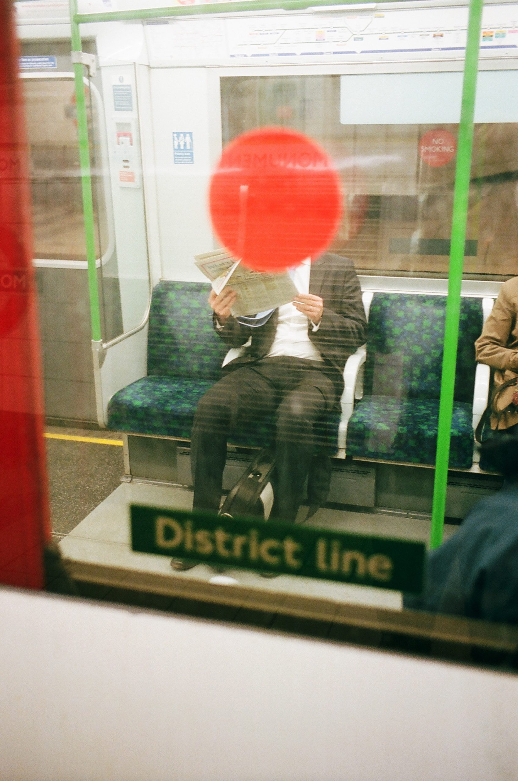 Red dot overlapped with man in suit. London tube, by Eric Kim