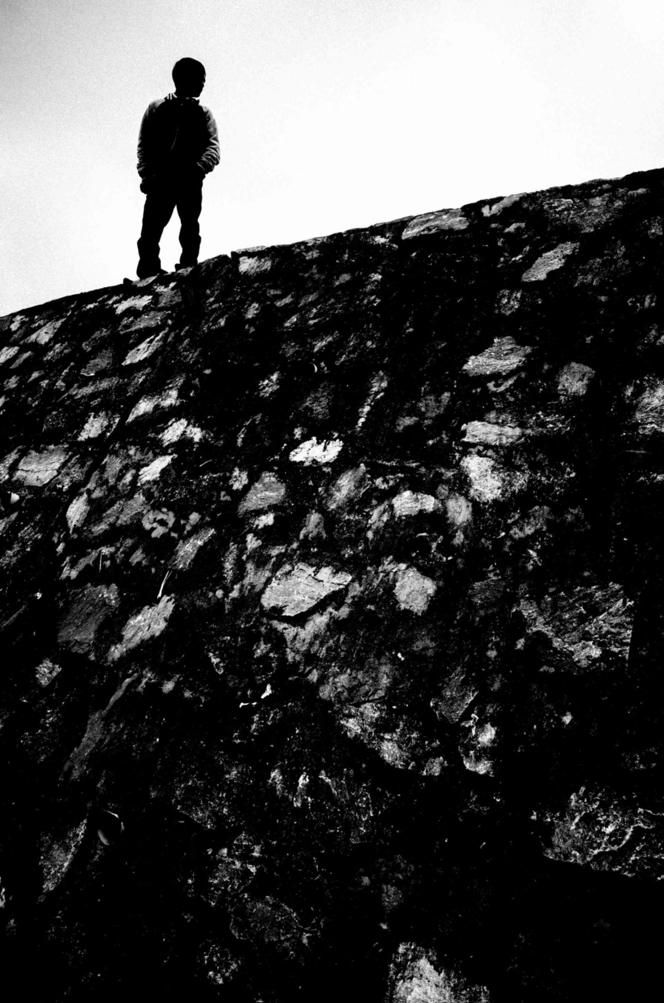 Simple figure to ground composition. Man in silhouette in black in top left of frame against white sky.